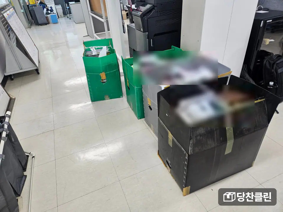 복합기 옆 바닥에 서류를 담은 상자 네 개가 놓인 사무실