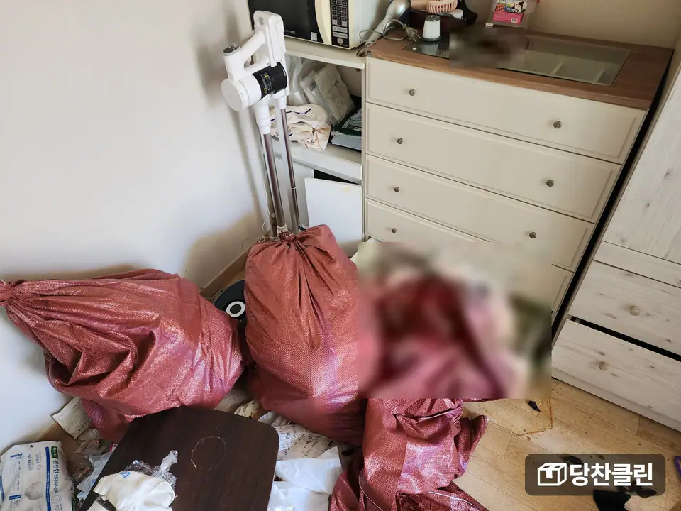 서랍장 옆에 마대 자루 세 개를 묶어 세워 두었고 바닥에 아직 담지 않은 물건이 남은 방